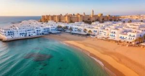 Piaszczysta plaża w Hammamet z turkusową wodą, tradycyjną białą zabudową i mediną w tle w promieniach zachodzącego słońca.