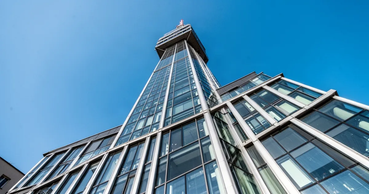 Szklana wieża Sky Tower we Wrocławiu widziana z poziomu ulicy, pnąca się ku bezchmurnemu błękitnemu niebu.