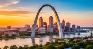 Panorama St. Louis z łukiem Gateway Arch nad rzeką Missisipi w ciepłym świetle zachodzącego słońca.