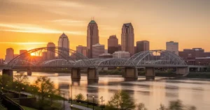 Panorama Cincinnati o zachodzie słońca z charakterystycznymi mostami i rzeką Ohio w ciepłych barwach.