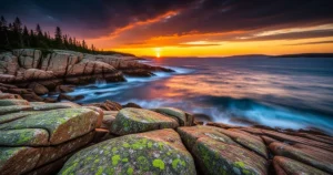Skaliste wybrzeże Parku Narodowego Acadia w Maine o wschodzie słońca z mchem na granitowych głazach i błękitem oceanu.